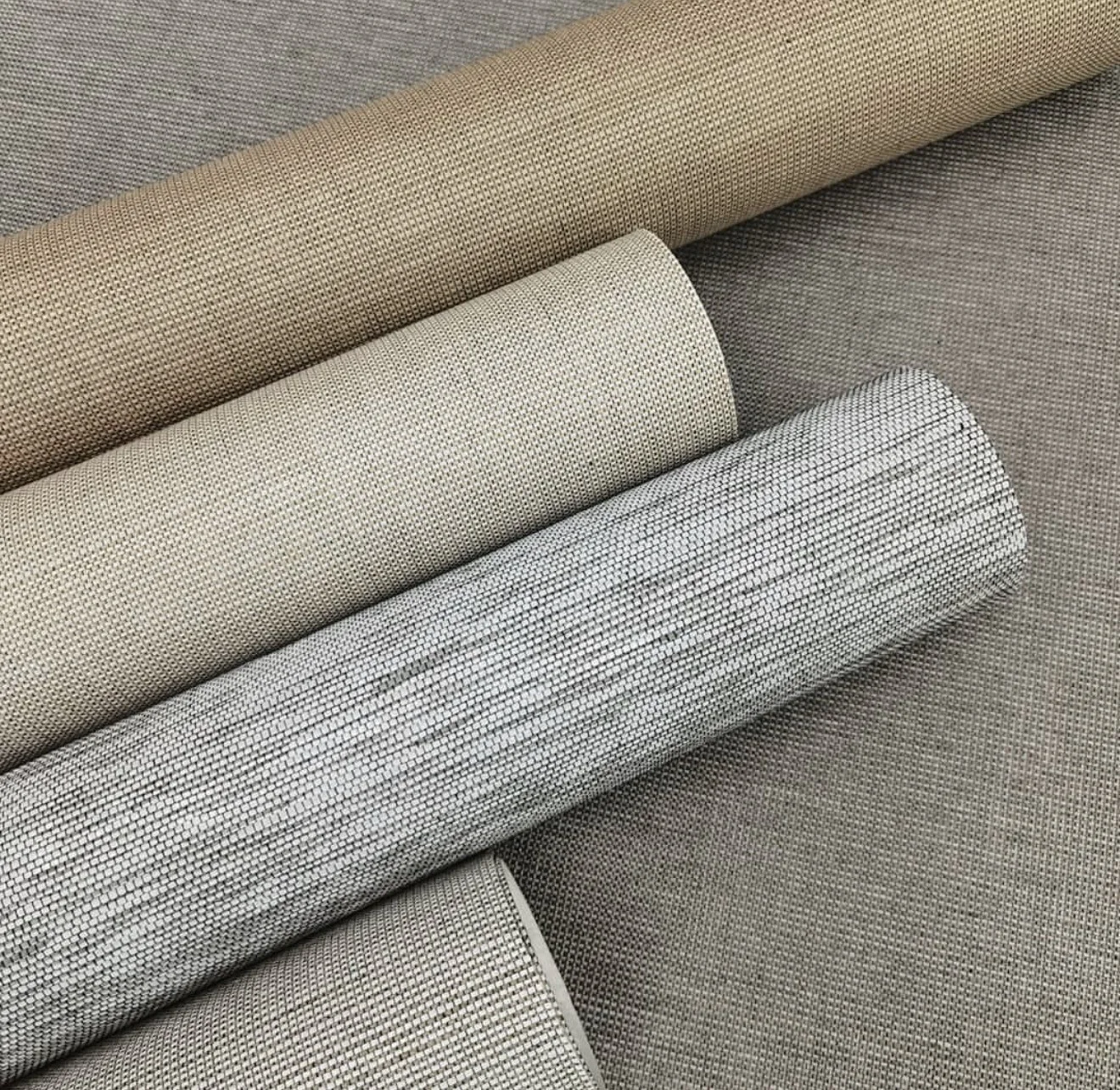 Rolls of woven natural wallcovering in sand, oatmeal and silver-grey tones showing fine fibre texture
