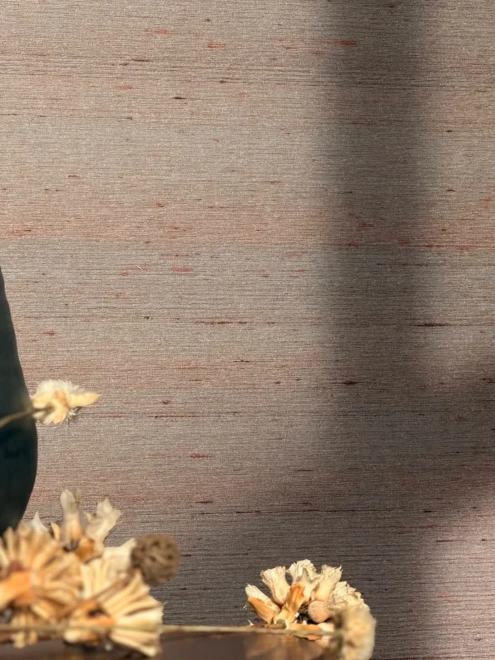 Taupe silk wallcovering with fine horizontal slubs and copper flecks behind a dark vase and dried flowers, crossed by soft shadow