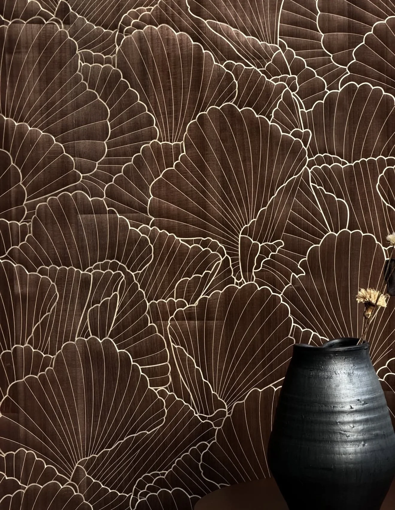 Bespoke dark walnut-toned wallcovering with an overlapping fan-shell motif outlined in fine gold line, beside a black ceramic vase