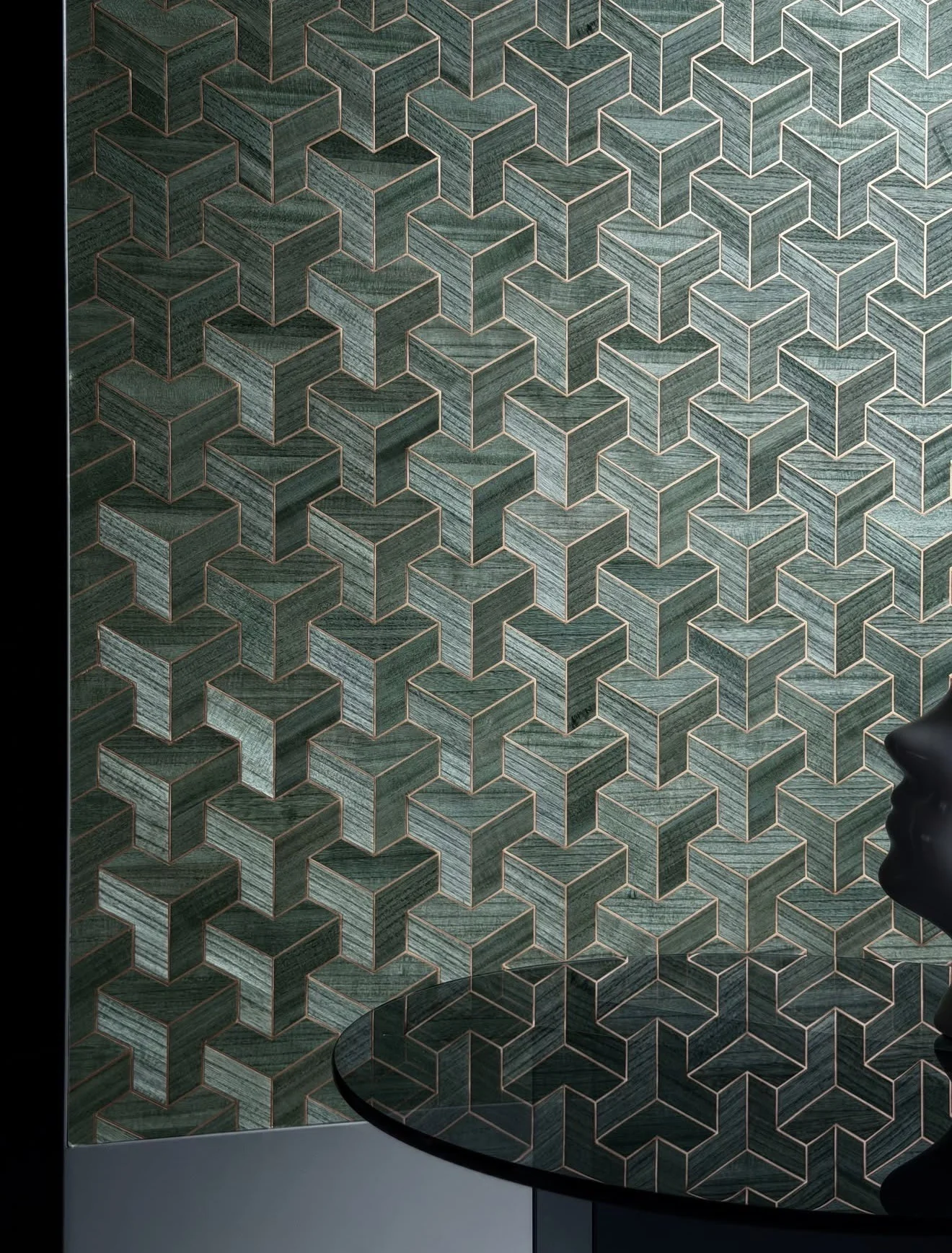 Deep green geometric wallcovering with interlocking gold-outlined forms, beside a dark curved table