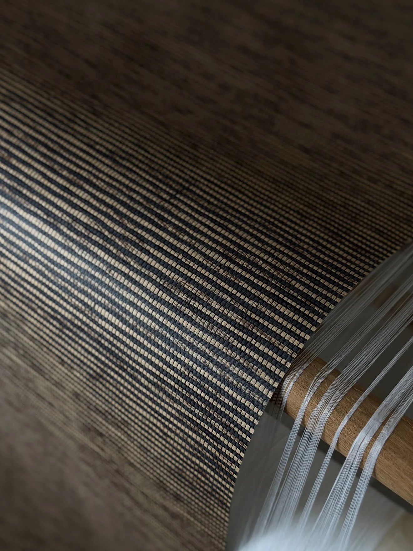 Close-up of a finely woven natural surface with dark and pale fibres and loose threads at its edge