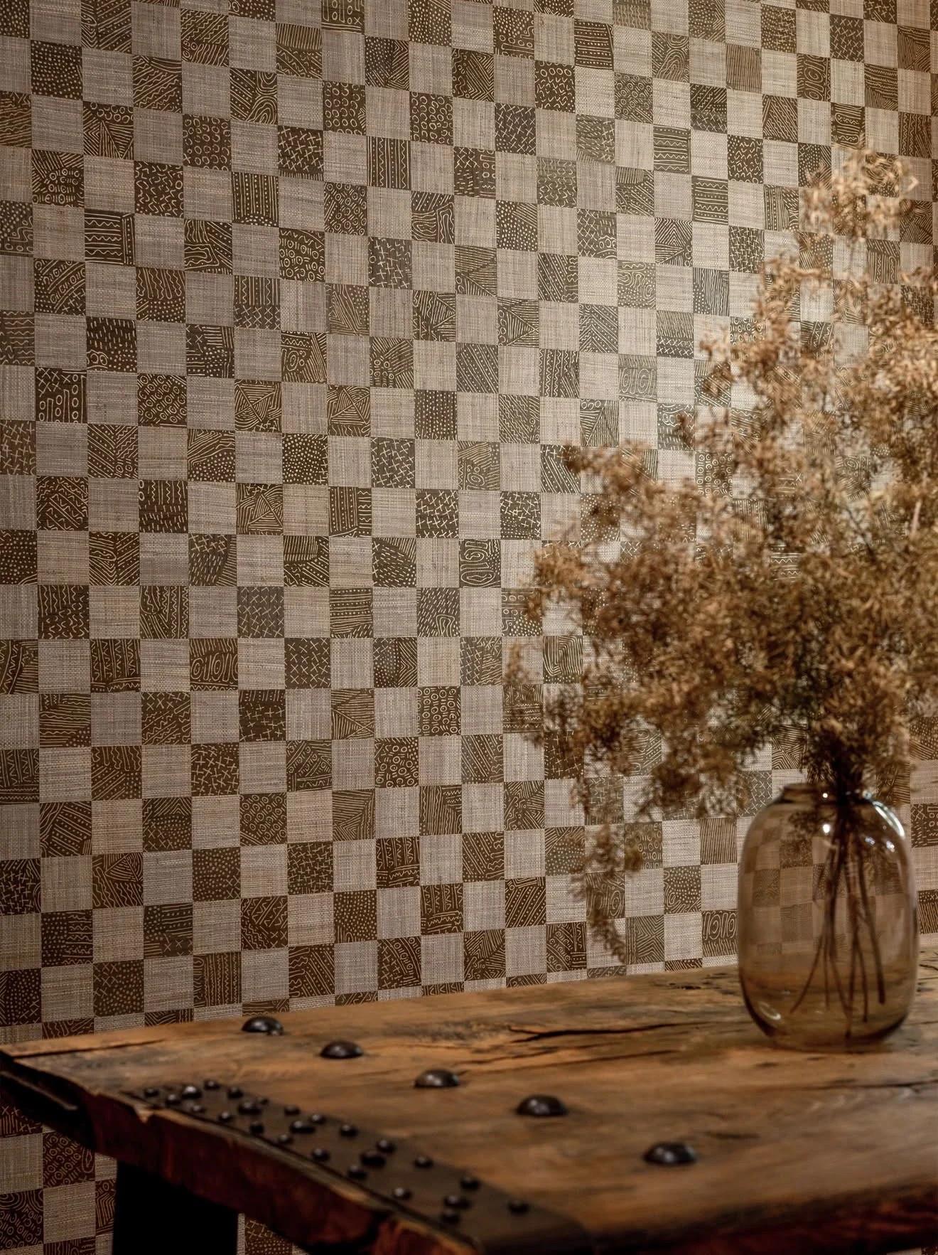 Brown and taupe patchwork wallcovering with fine contrasting patterns, behind an amber vase and timber table