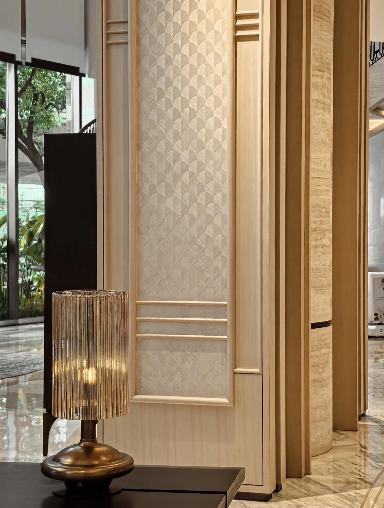 Cream geometric wallcovering within pale architectural panelling beside a bronze table lamp
