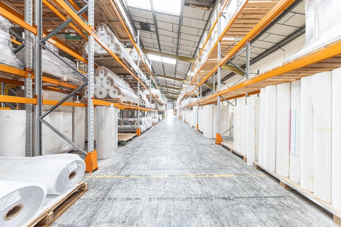 Long aisle of the John Mark manufacturing and storage facility, with wallcovering rolls racked high on both sides