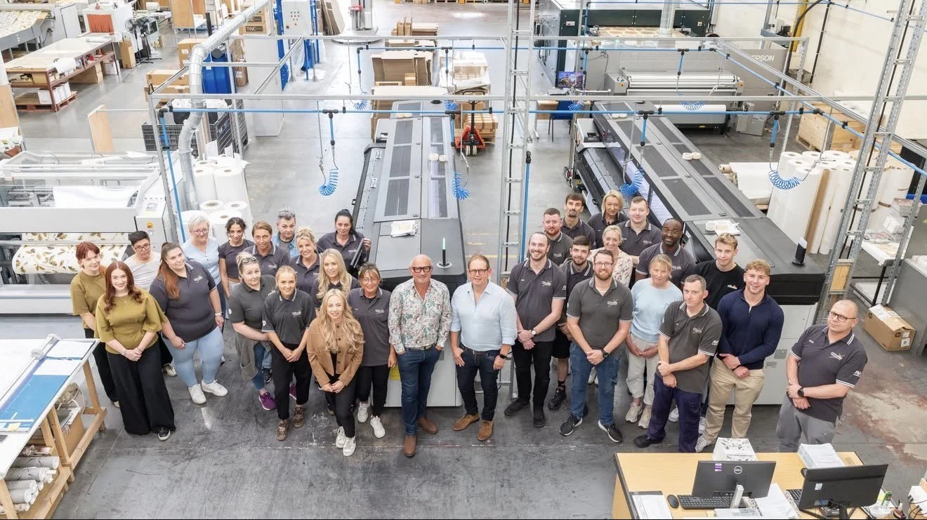 The John Mark team gathered on the factory floor in Leyland, Lancashire, between large-format digital wallcovering printers
